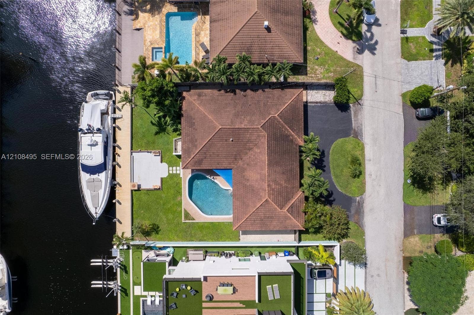 3080 NE 43rd Street, Fort Lauderdale, FL 33308 Aerial perspective of a waterfront property featuring a canal-front bulkhead, private swimming pool, concrete patio, paved driveway, and tile roof