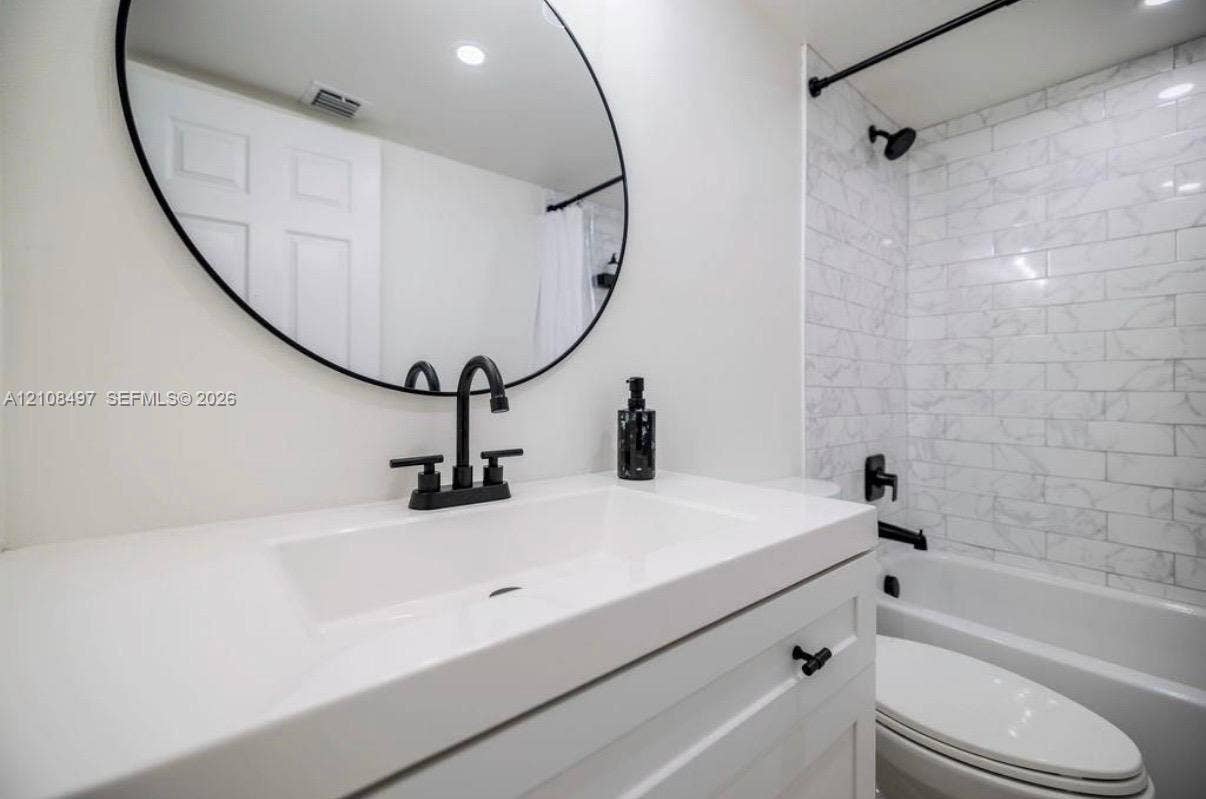6245 SW 47th Manor, #101, Davie, FL 33314 White vanity with a rectangular sink, matte black faucet, oval wall-mounted mirror, and a tub-shower combination featuring subway-tile wall surround