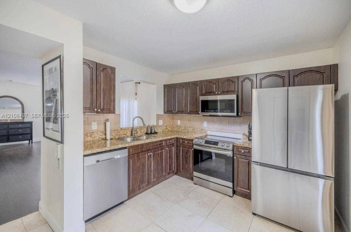 6245 SW 47th Manor, #101, Davie, FL 33314 Kitchen featuring dark wood cabinetry, stone-surface countertops, tile backsplash, and stainless steel appliances including a refrigerator, range, microwave, and dishwasher