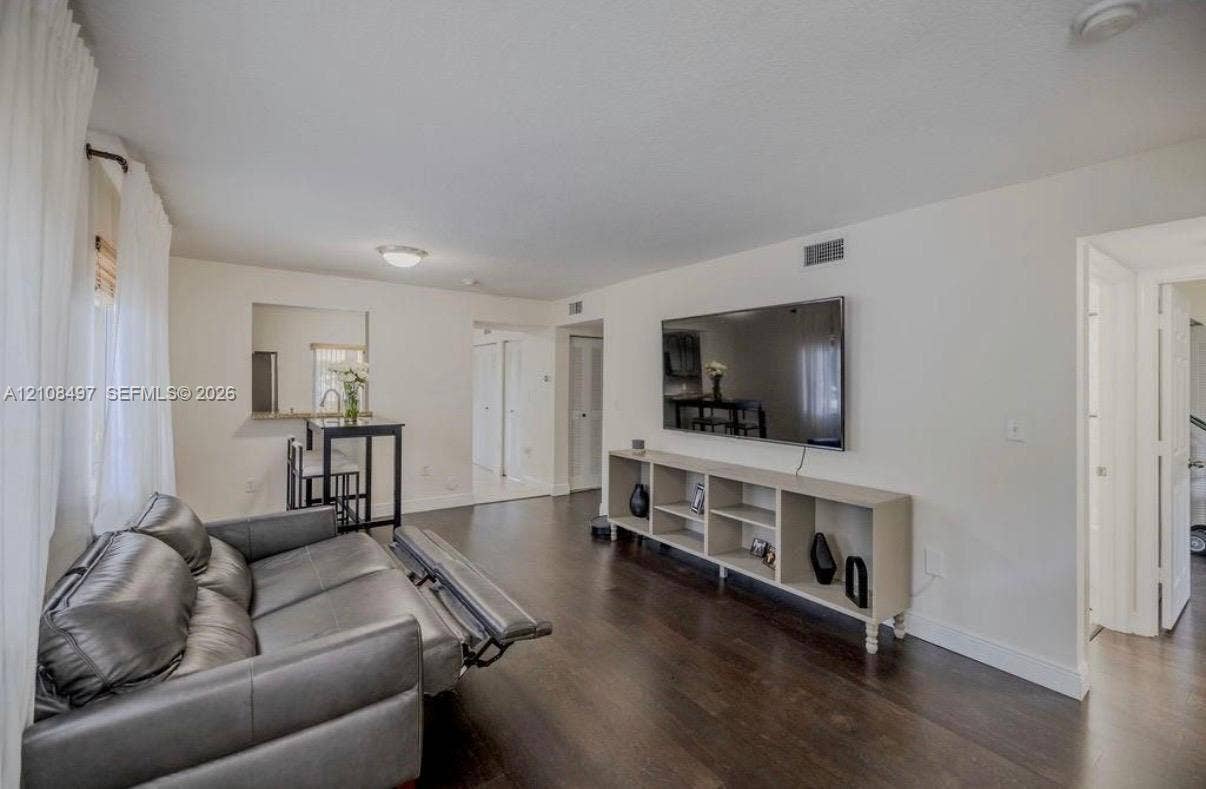 6245 SW 47th Manor, #101, Davie, FL 33314 Living area featuring dark wood-finish flooring, neutral wall tones, a recessed wall niche, and an interior pass-through window with a ledge