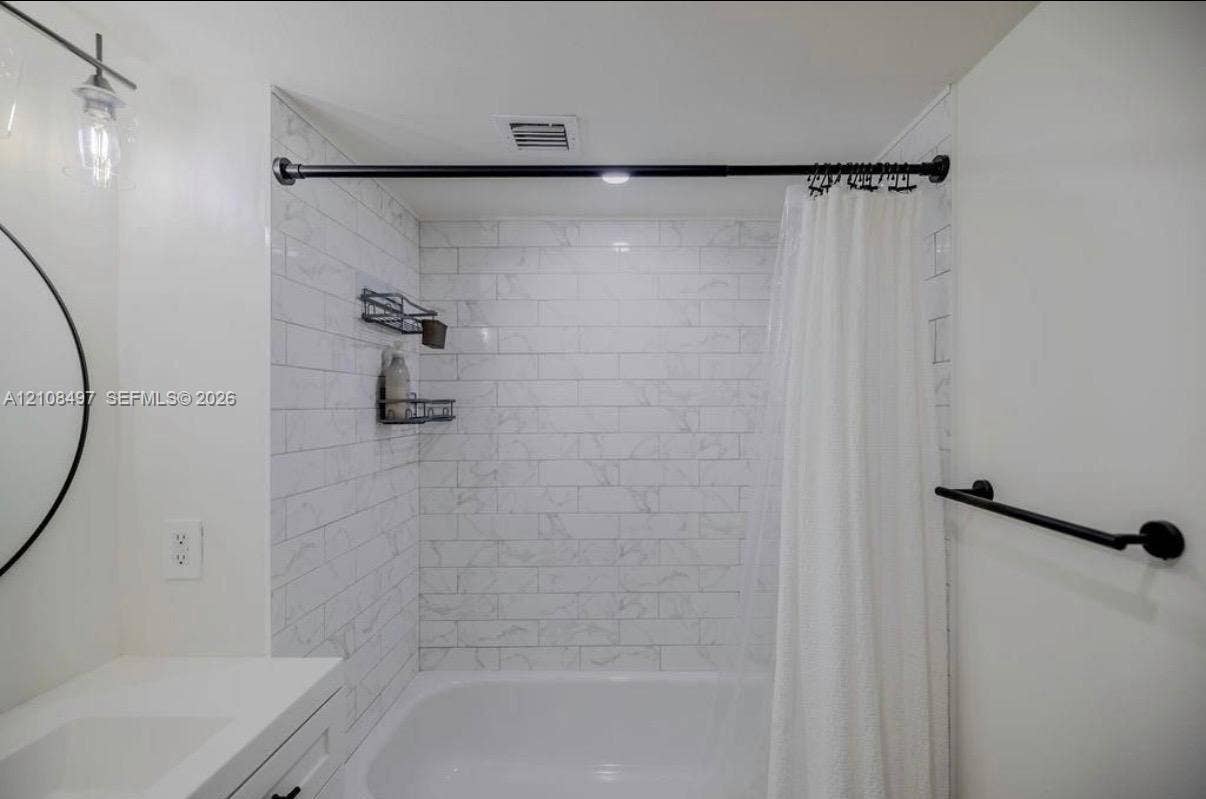 6245 SW 47th Manor, #101, Davie, FL 33314 Full bathroom featuring a tub-shower combination with white subway-style tiling, a vanity with a white countertop, a circular wall-mounted mirror, and matte black fixtures