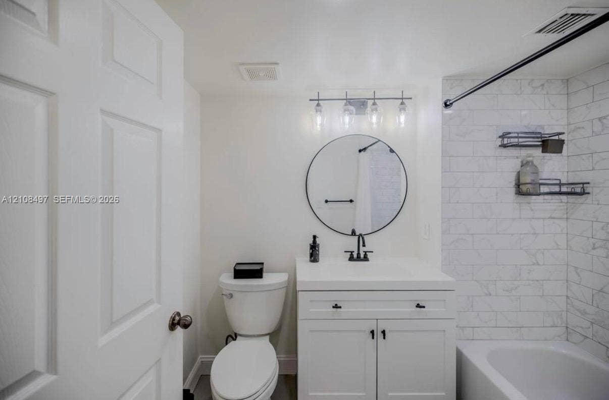 6245 SW 47th Manor, #101, Davie, FL 33314 Bathroom featuring a vanity with integrated sink, circular wall-mounted mirror, matte black hardware, and tub surround with subway tile finish