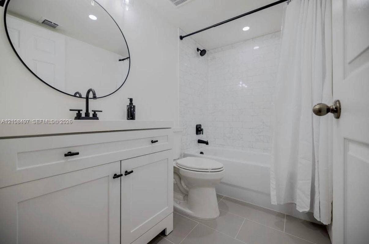 6245 SW 47th Manor, #101, Davie, FL 33314 White vanity featuring matte black hardware and a circular mirror, paired with a shower-tub combination finished in white subway tile and matte black fixtures, complemented by large-format tile flooring