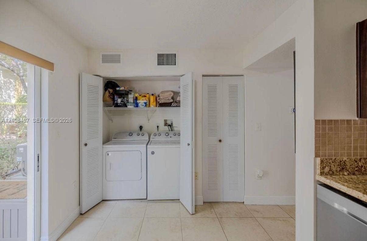 6245 SW 47th Manor, #101, Davie, FL 33314 Laundry closet featuring side-by-side appliances, overhead shelving, and louvered folding doors, complemented by tile flooring and an additional louvered-door closet