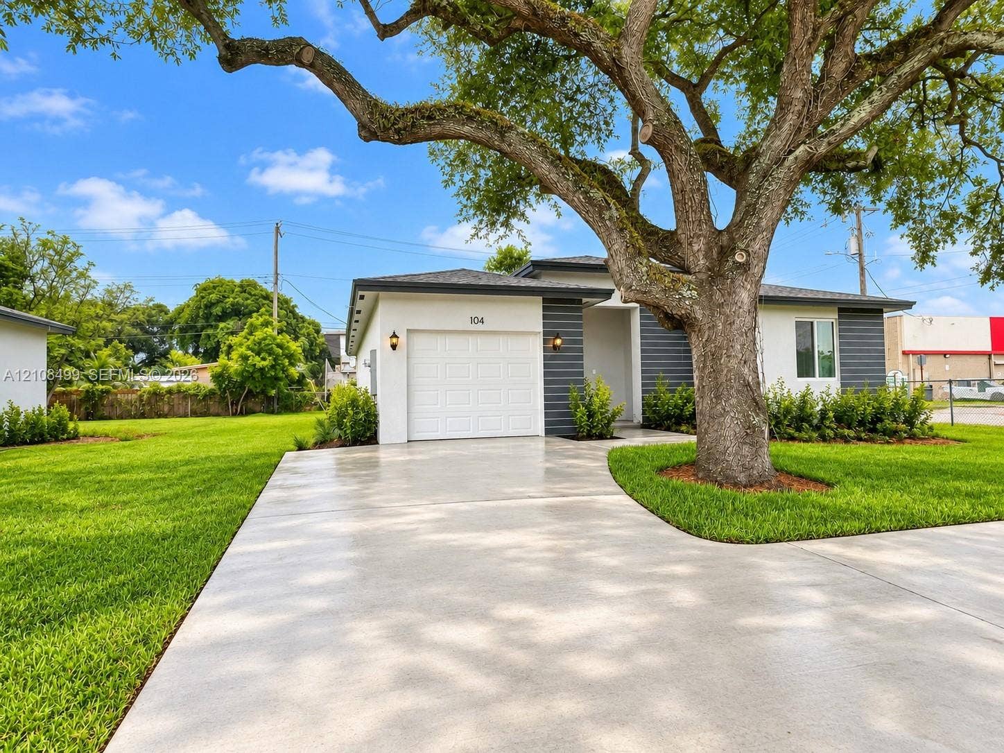 104 NW 31st Avenue, Fort Lauderdale, FL 33311 Exterior featuring light-colored stucco, contrasting dark grey horizontal siding, a single-car garage, an expansive lawn, and a mature shade tree