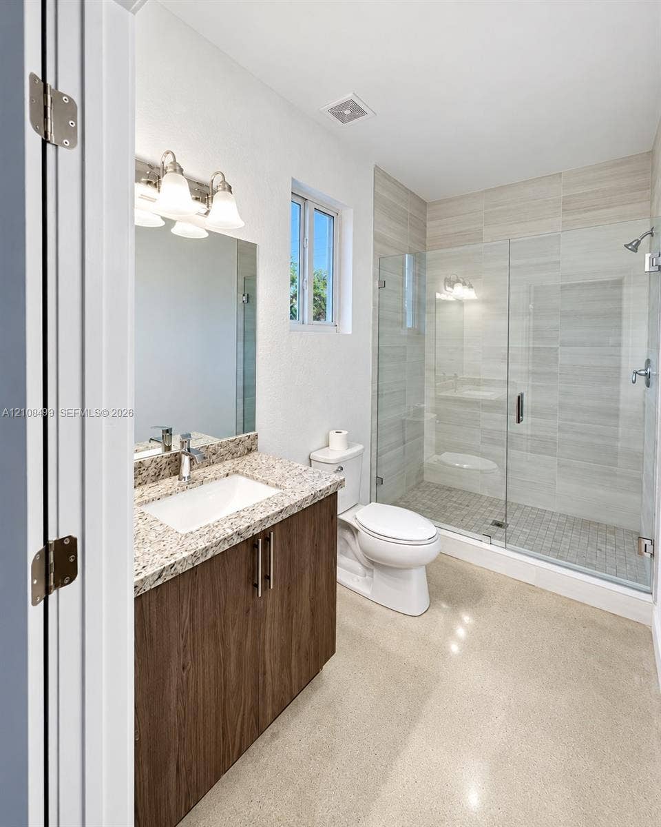 104 NW 31st Avenue, Fort Lauderdale, FL 33311 Bathroom featuring a wood-finish vanity with a stone countertop, an integrated rectangular sink, a glass-enclosed shower with tile surround, and polished concrete flooring