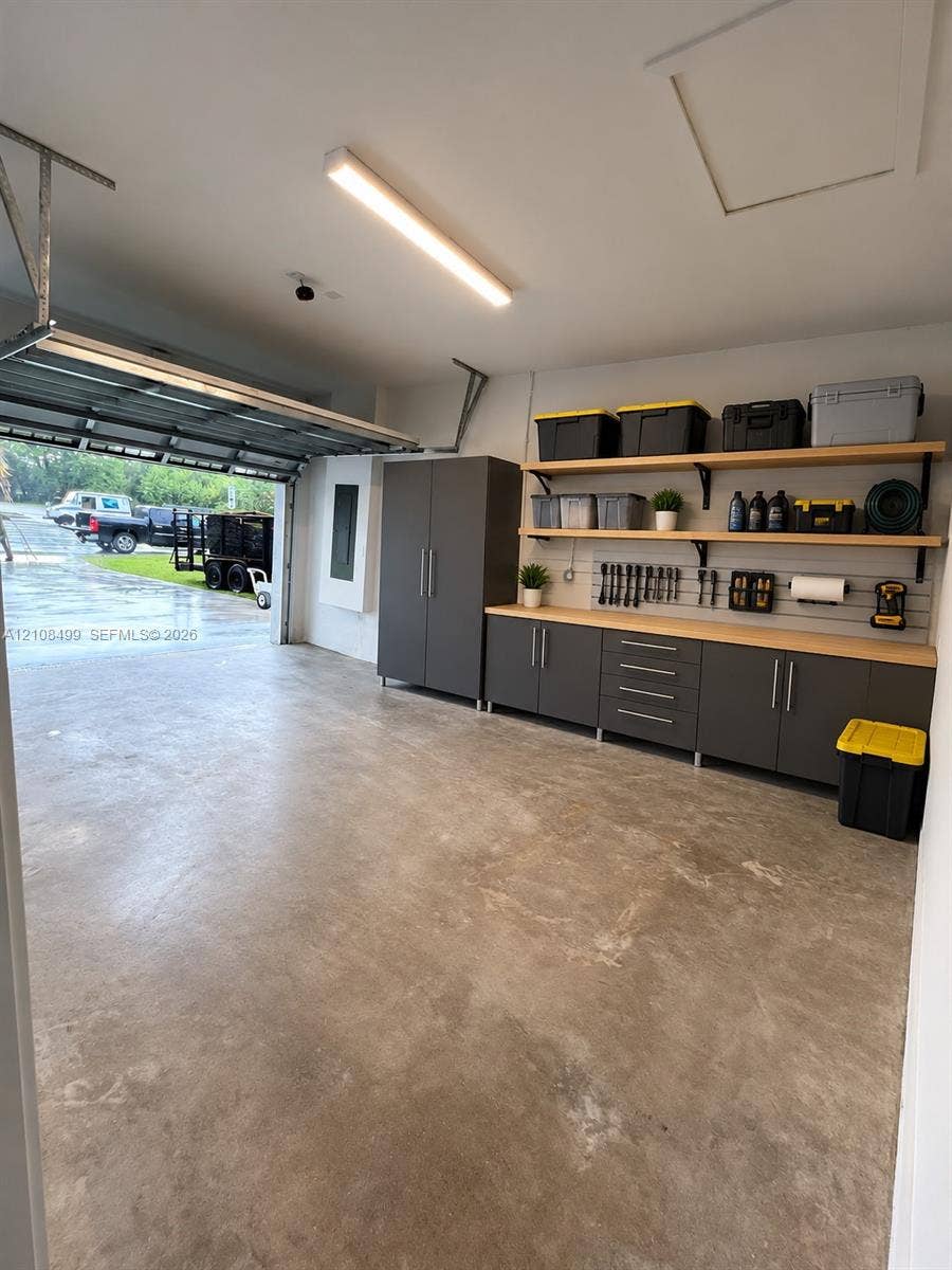 104 NW 31st Avenue, Fort Lauderdale, FL 33311 Garage featuring custom floor-to-ceiling cabinetry, integrated wall-mounted slat organization, wood-surfaced built-in workbench, and overhead linear lighting
