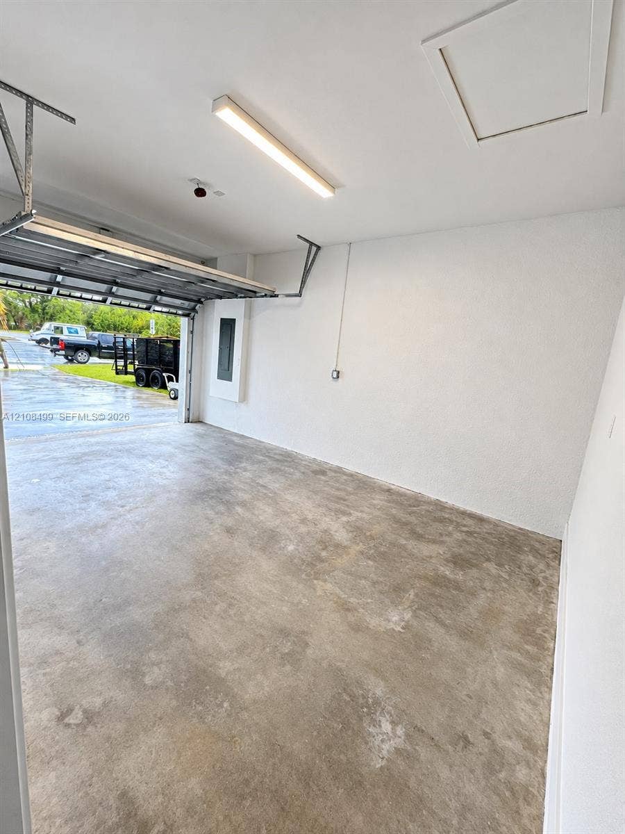104 NW 31st Avenue, Fort Lauderdale, FL 33311 Finished garage featuring smooth-texture walls, a concrete floor, a linear LED light fixture, and an attic access panel