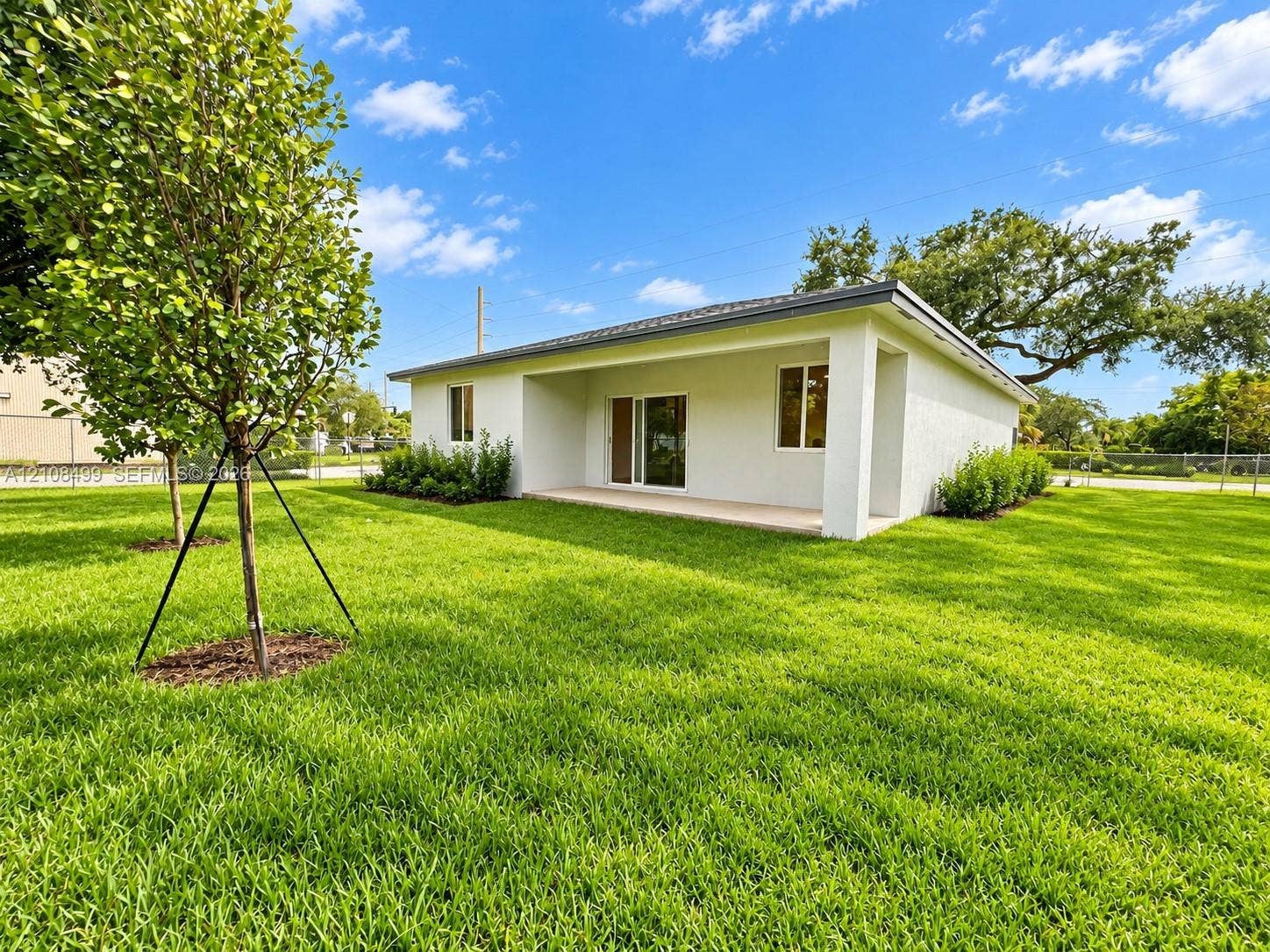 104 NW 31st Avenue, Fort Lauderdale, FL 33311 Stucco exterior featuring a covered patio, sliding glass door, and expansive grass lawn with mature trees