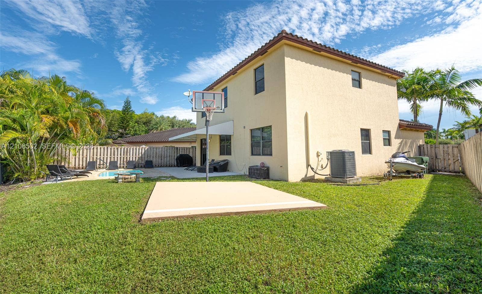 Backyard featuring a stucco-exterior residence, a concrete patio, an in-ground swimming pool, a dedicated basketball court, and perimeter wood fencing