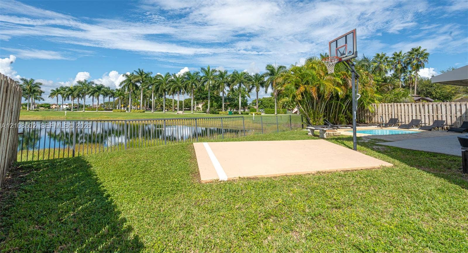 180 NE 26th Avenue, Homestead, FL 33033 Backyard featuring a paved basketball court, swimming pool, fenced perimeter, and waterfront scenery