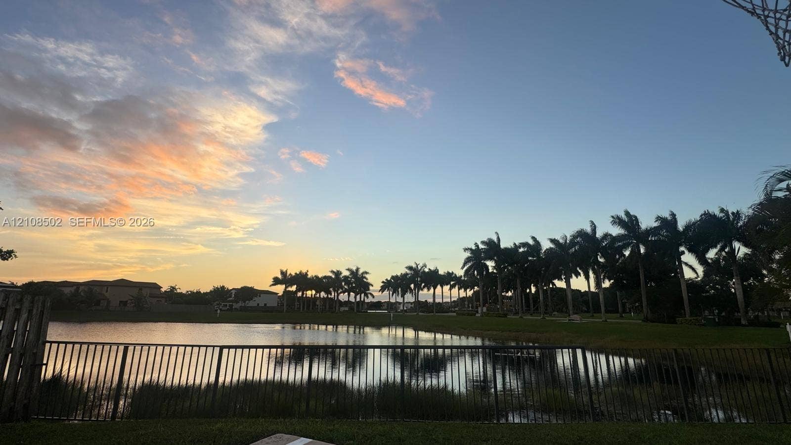 180 NE 26th Avenue, Homestead, FL 33033 Waterfront property featuring a metal perimeter fence, manicured lawn, and mature palm trees