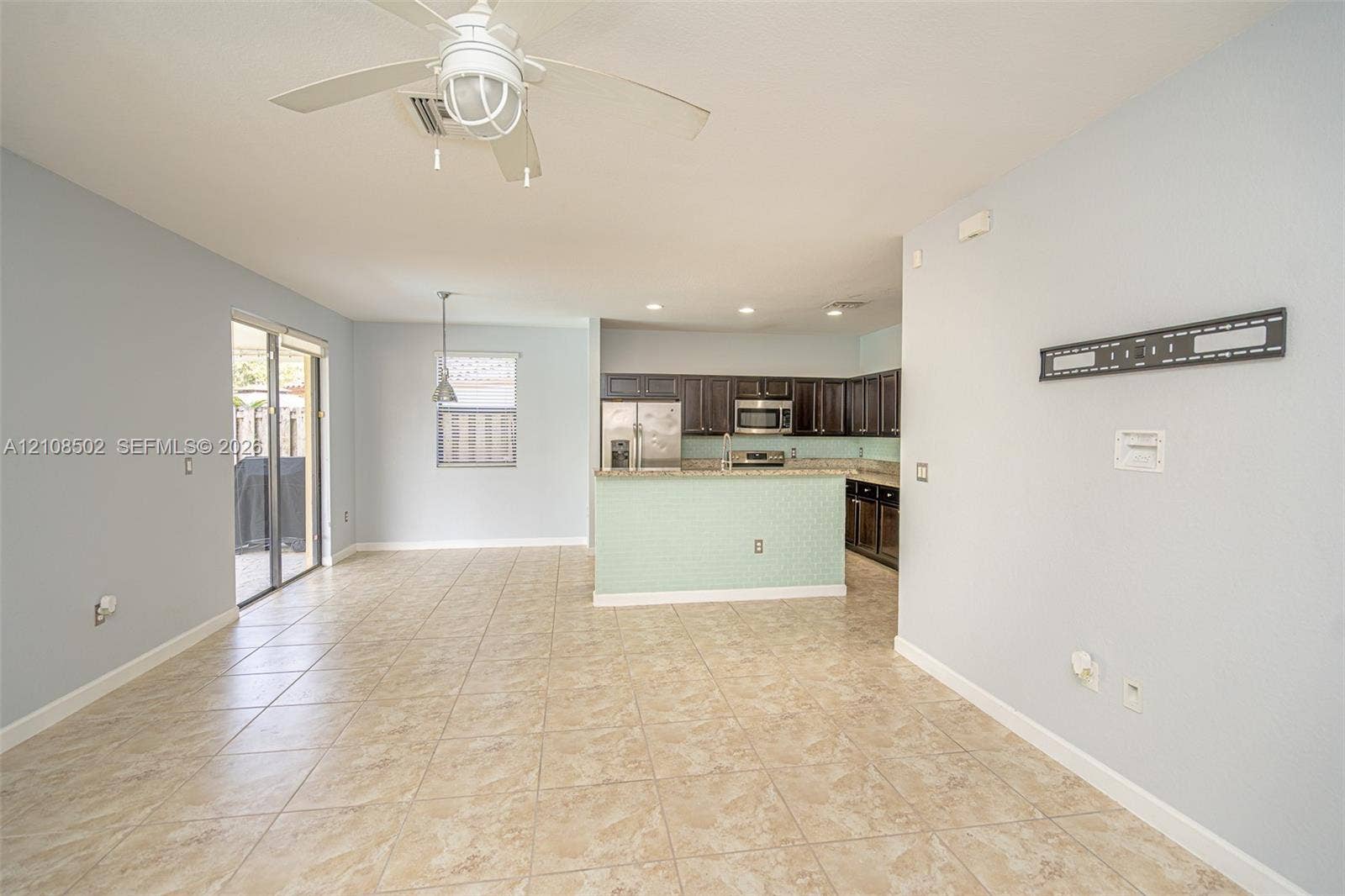 Open-concept interior featuring tile flooring, a kitchen peninsula with a tiled front, dark-finish cabinetry, built-in stainless steel appliances, and a ceiling fan with integrated lighting