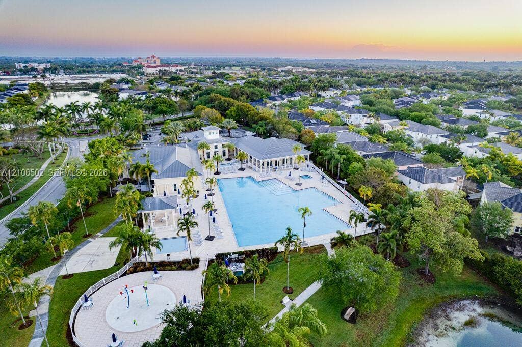 Community recreation complex featuring a large swimming pool, splash pad, and surrounding hardscaped lounging areas situated within a landscaped environment