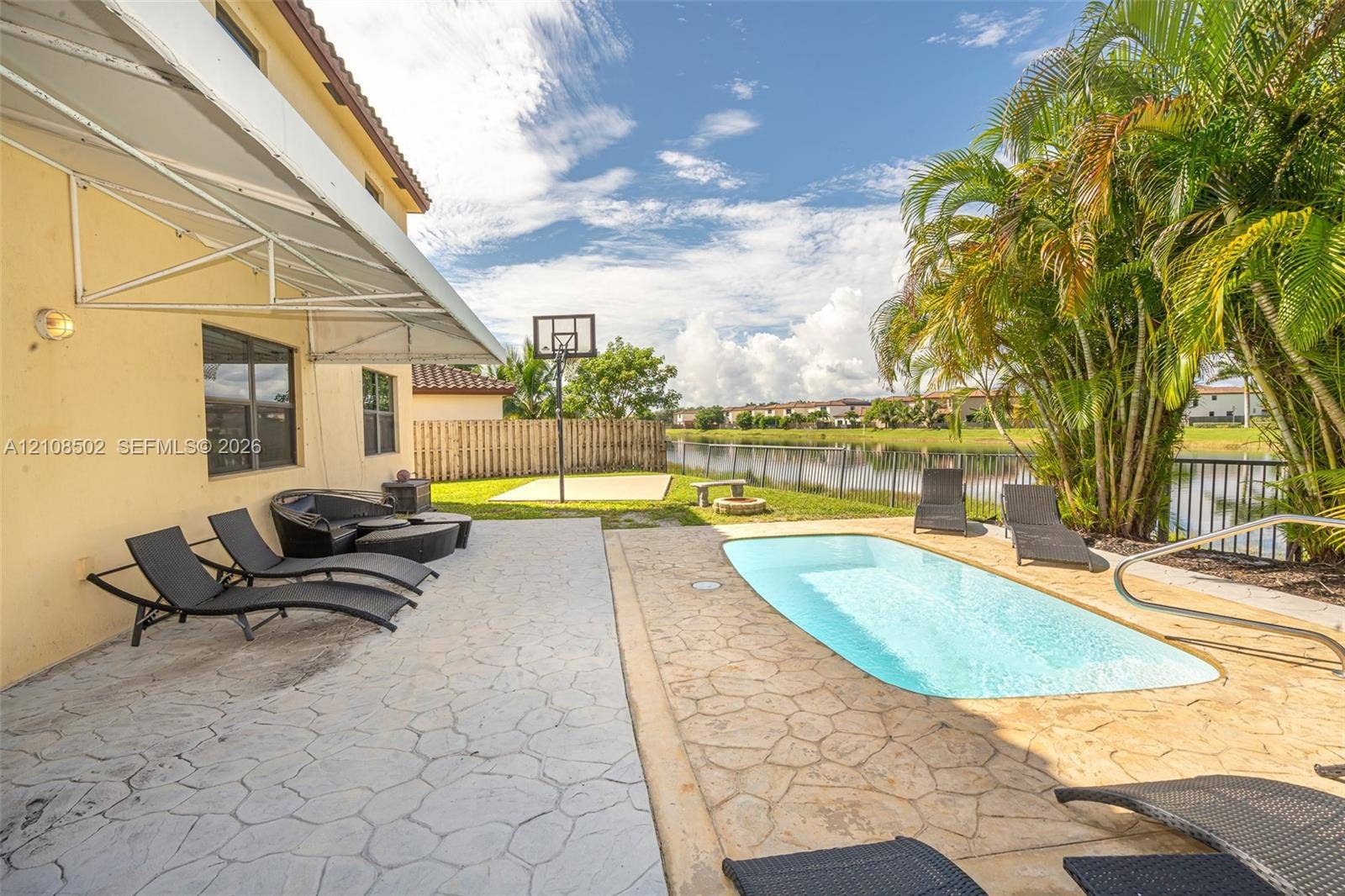 Outdoor living area featuring a paved patio, swimming pool, basketball court, and water frontage