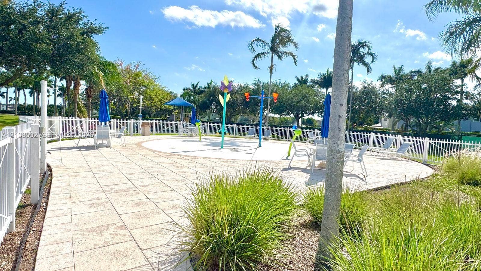 180 NE 26th Avenue, Homestead, FL 33033 Outdoor splash pad featuring water features, paved patio decking, white perimeter fencing, and mature palm trees