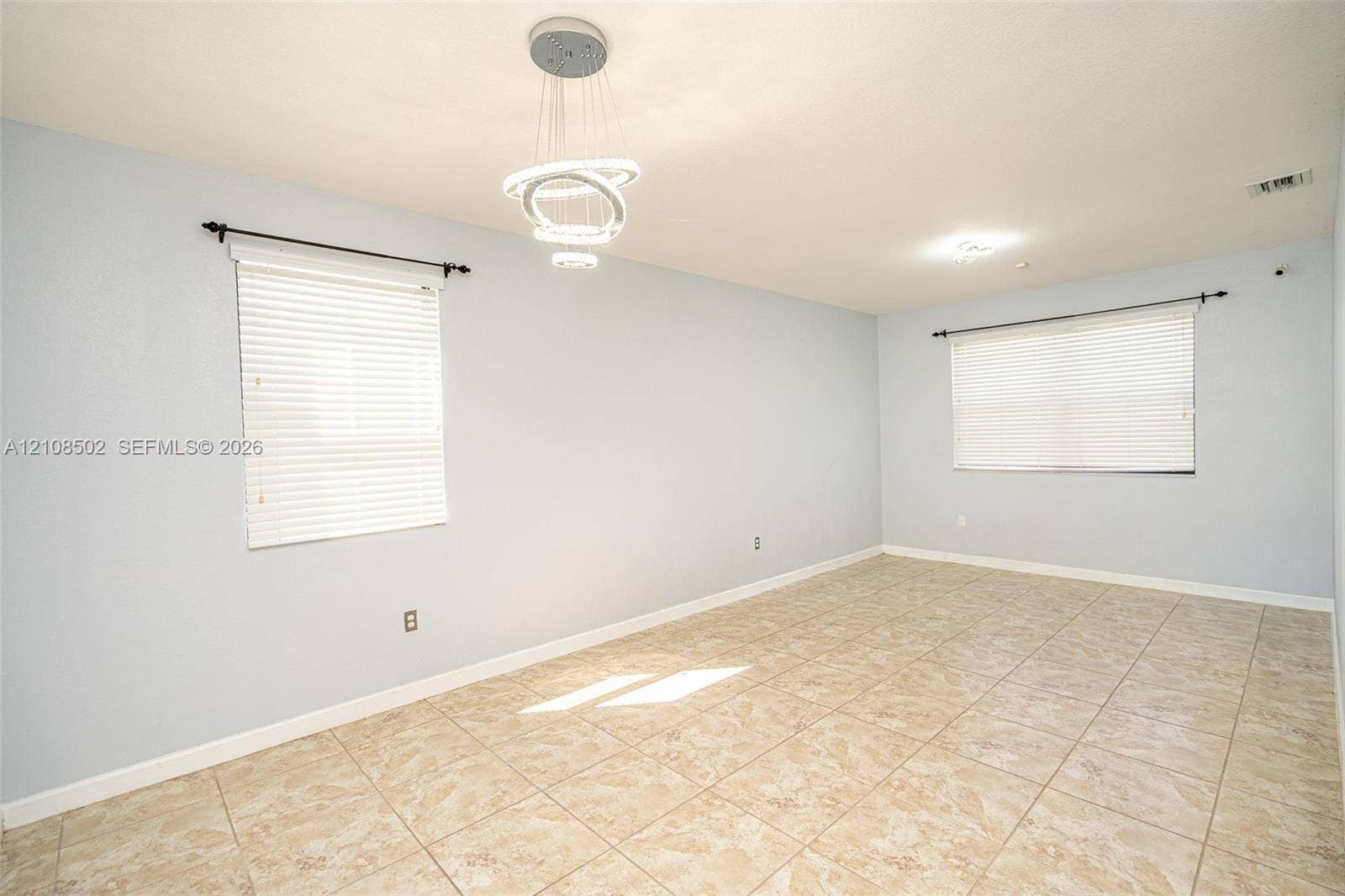 180 NE 26th Avenue, Homestead, FL 33033 Interior space featuring ceramic tile flooring, neutral wall paint, modern multi-ring LED pendant lighting, and two windows with installed blinds