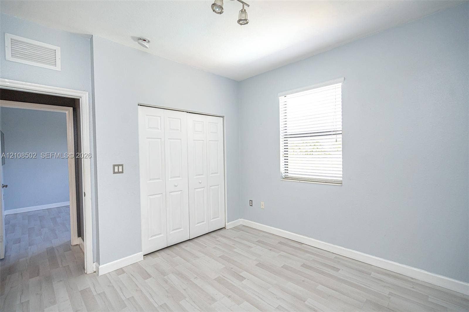 180 NE 26th Avenue, Homestead, FL 33033 Room featuring wood-finish flooring, a double-panel closet with white doors, a single window with horizontal blinds, and a multi-bulb ceiling-mounted light fixture