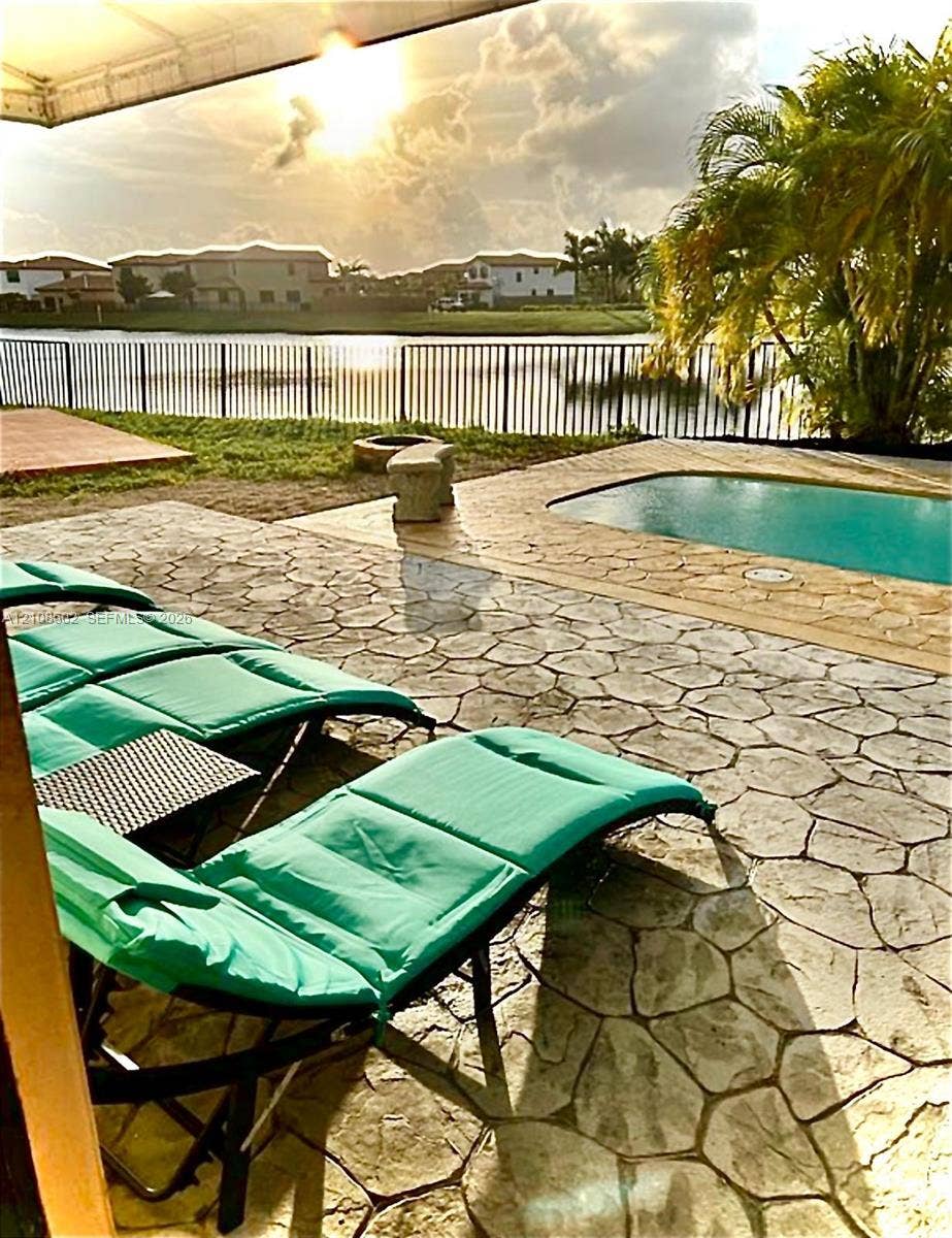 Outdoor living area featuring a stamped concrete patio, in-ground swimming pool, metal perimeter fencing, and water frontage
