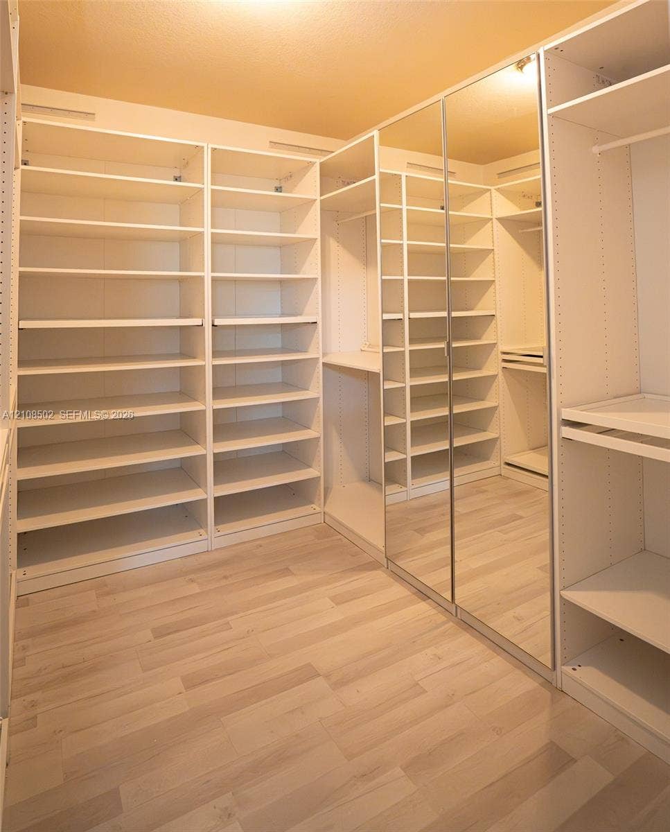 180 NE 26th Avenue, Homestead, FL 33033 Walk-in closet featuring extensive built-in shelving, full-length mirrored door panels, wood-finish flooring, and integrated garment rods