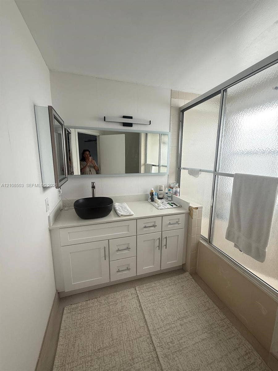 4872 NW 97th Place, #289, Doral, Doral, FL 33178 White cabinetry vanity featuring a solid surface countertop, matte black vessel sink, wall-mounted rectangular mirror, and a sliding glass shower door