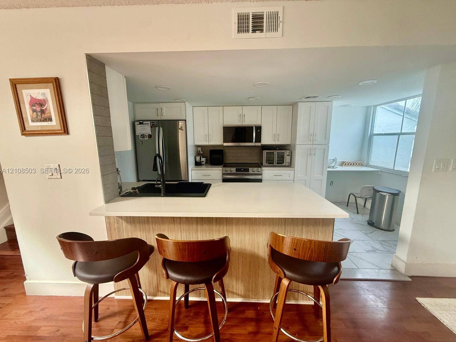 4872 NW 97th Place, #289, Doral, Doral, FL 33178 Kitchen featuring white cabinetry, solid-surface countertops, integrated stainless steel appliances, a black undermount sink with a matte black faucet, and wood-finish cabinetry detailing