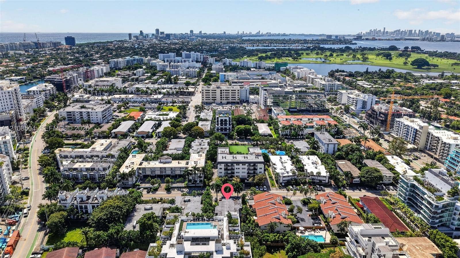 Aerial perspective of a multi-unit residential property featuring paved on-site parking, mature palm trees, and proximity to coastal waterways and urban infrastructure