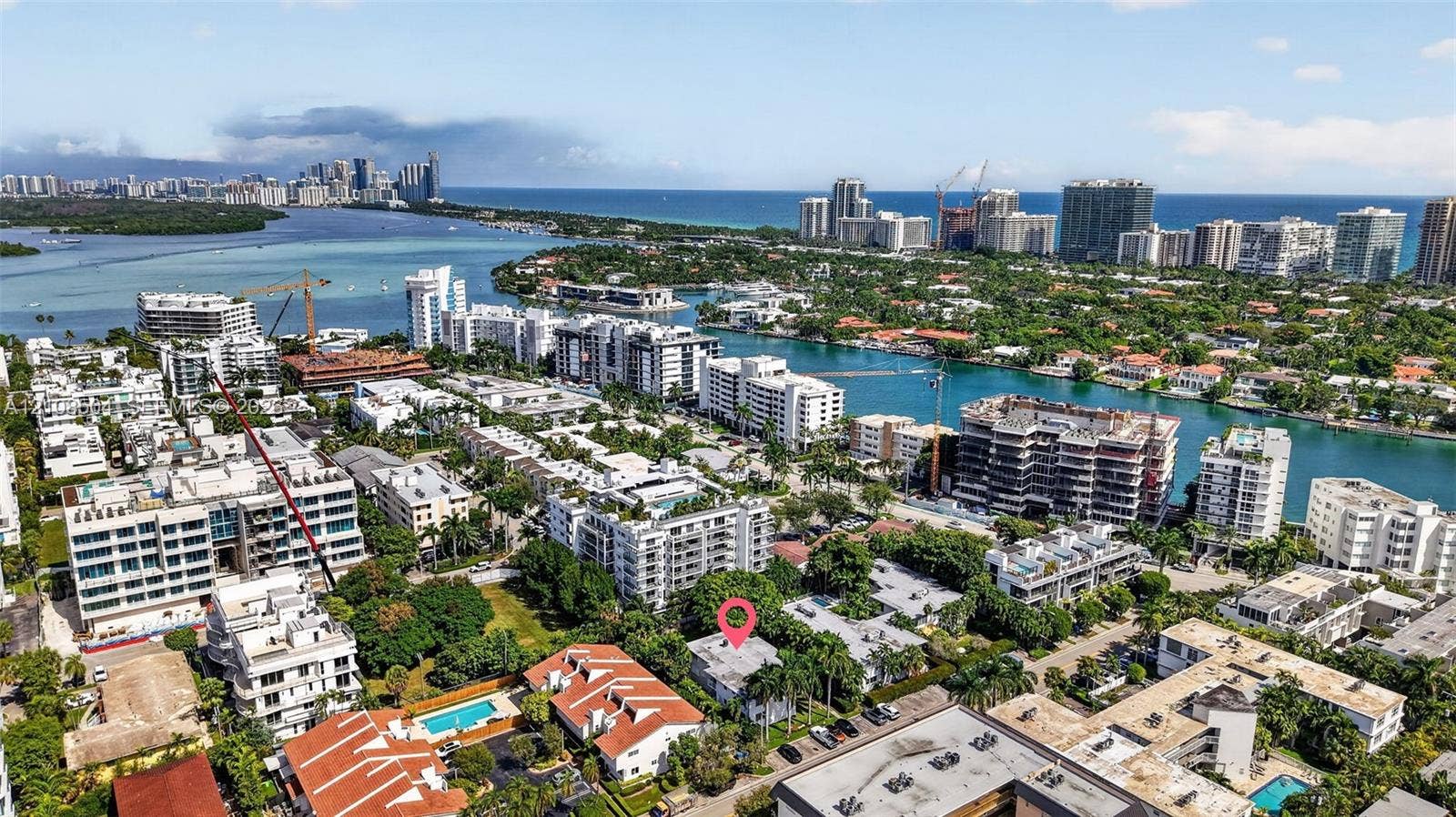 Aerial perspective of a coastal residential area featuring mature landscaping, proximity to waterfront channels, and urban skyline backdrops