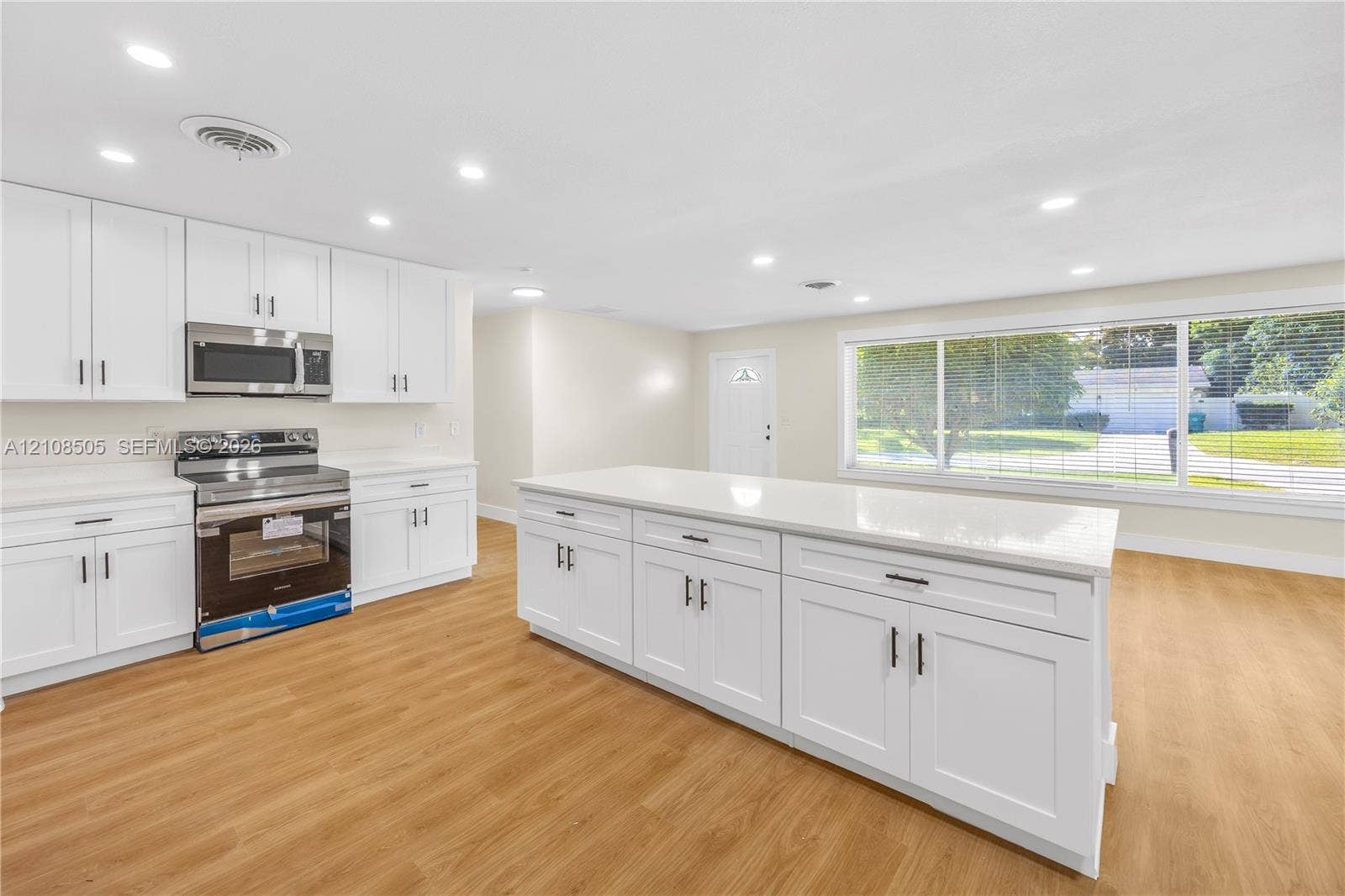 Kitchen featuring white shaker-style cabinetry, a quartz-topped center island, wood-finish flooring, recessed lighting, and stainless steel appliances