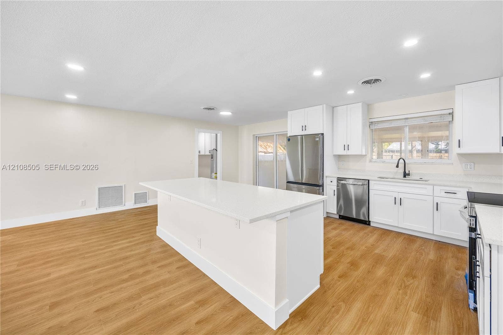 Kitchen featuring white cabinetry, quartz countertops, a central island, stainless steel appliances, and wood-finish flooring