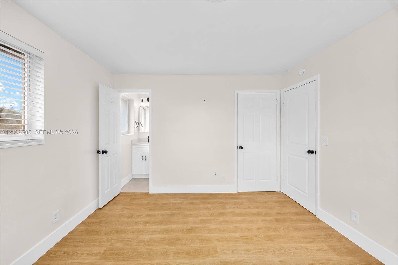 Room featuring wood-finish flooring, two white panel doors, and window with horizontal blinds