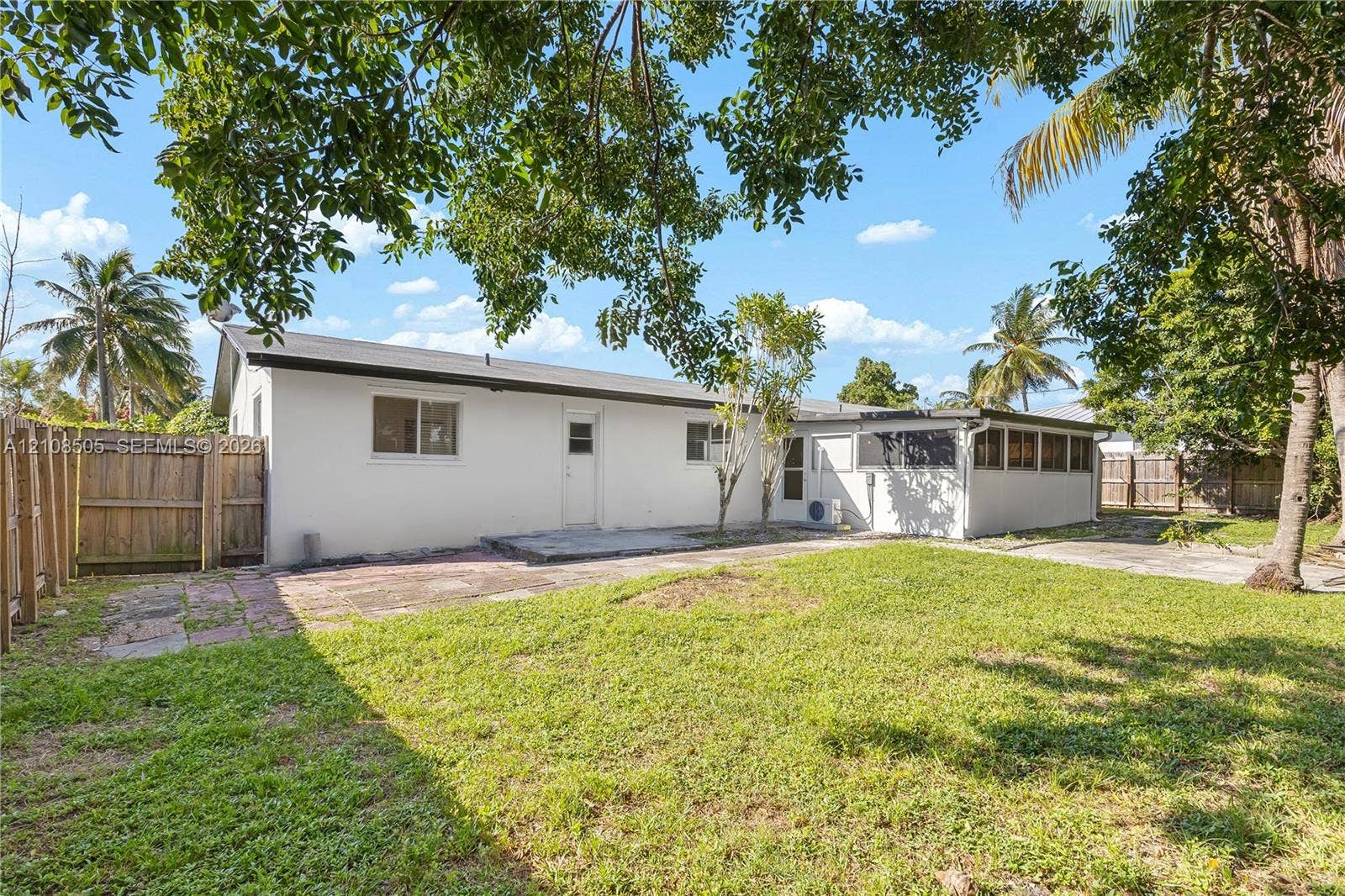 Exterior of residence featuring a concrete patio, wood privacy fencing, a manicured lawn, and mature palm trees