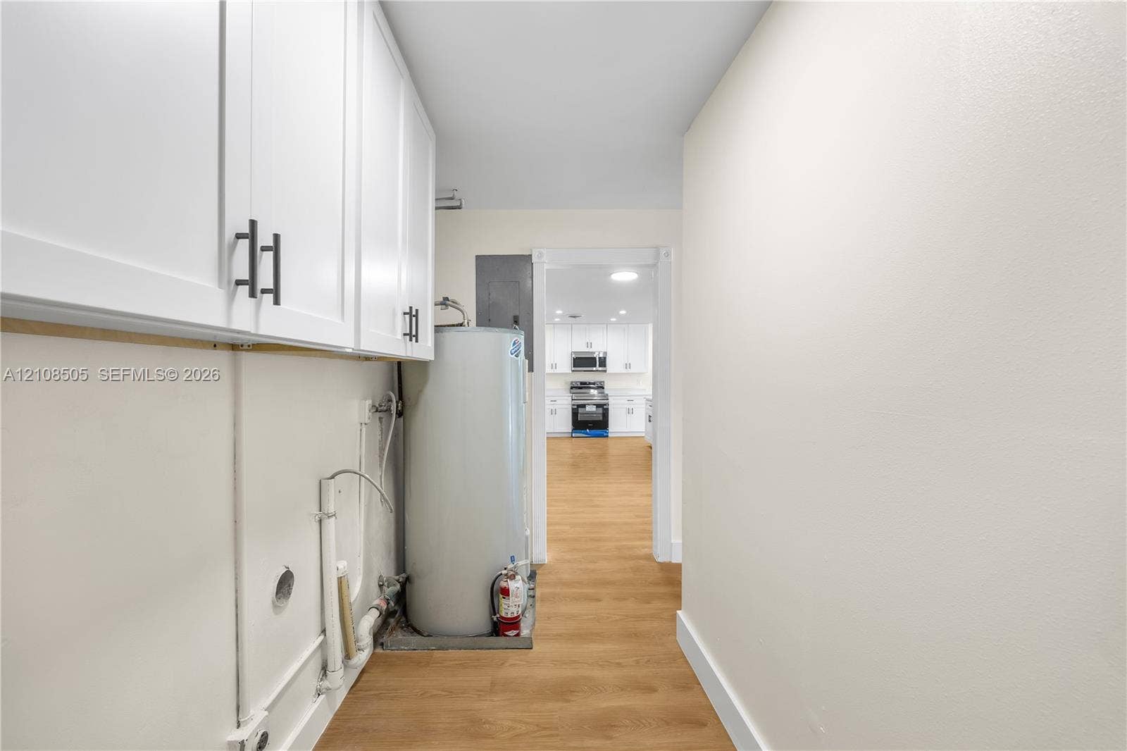 White cabinetry with matte black hardware, wood-finish flooring, and a water heater