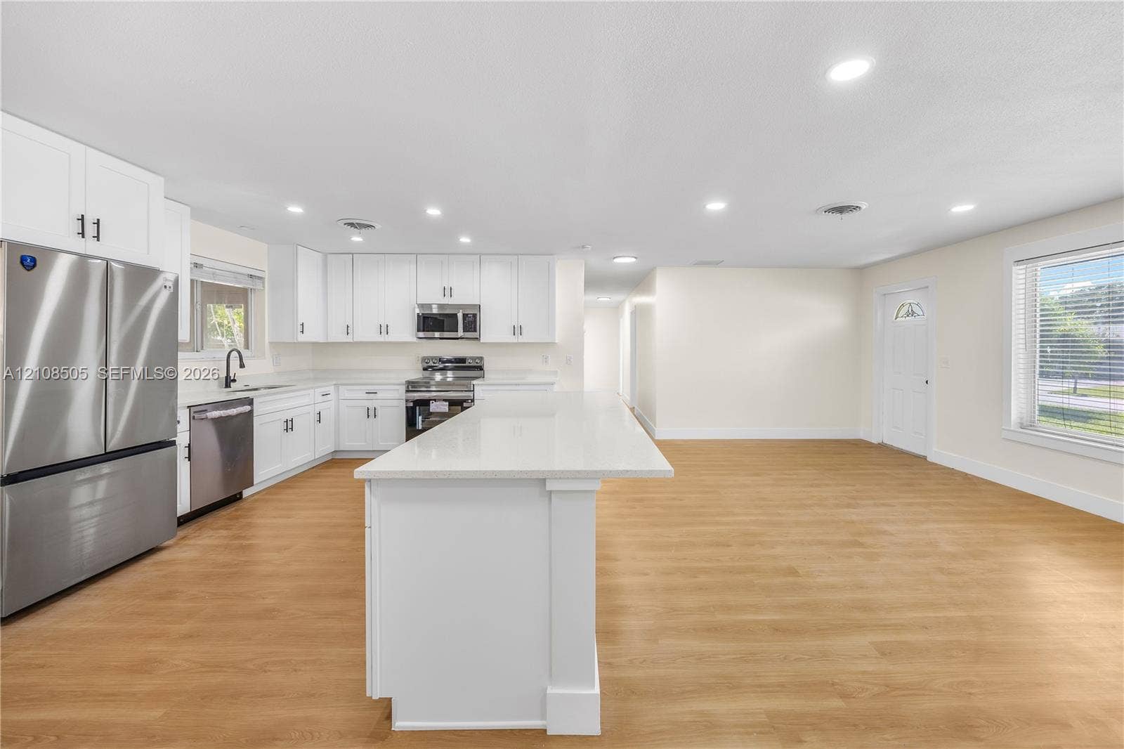 Kitchen featuring white cabinetry, an expansive central island with a solid-surface countertop, stainless steel appliances, and wood-finish flooring with recessed lighting
