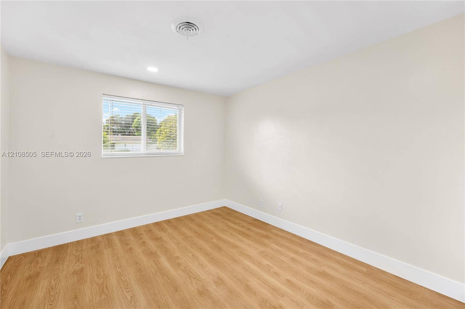 Neutral-toned interior space featuring wood-finish flooring, crisp white wall paint, and a single window with horizontal blinds