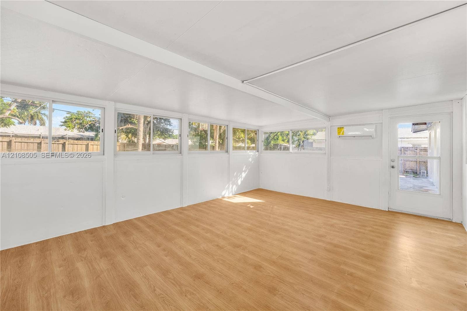 Enclosed room featuring wood-finish flooring, numerous sliding glass windows, white walls, and a wall-mounted ductless air conditioning unit
