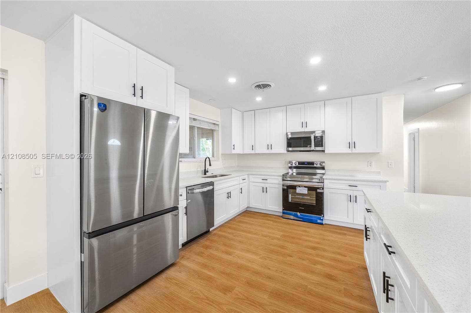 Kitchen featuring white shaker-style cabinetry, solid-surface countertops, wood-finish flooring, stainless steel appliances, and recessed lighting