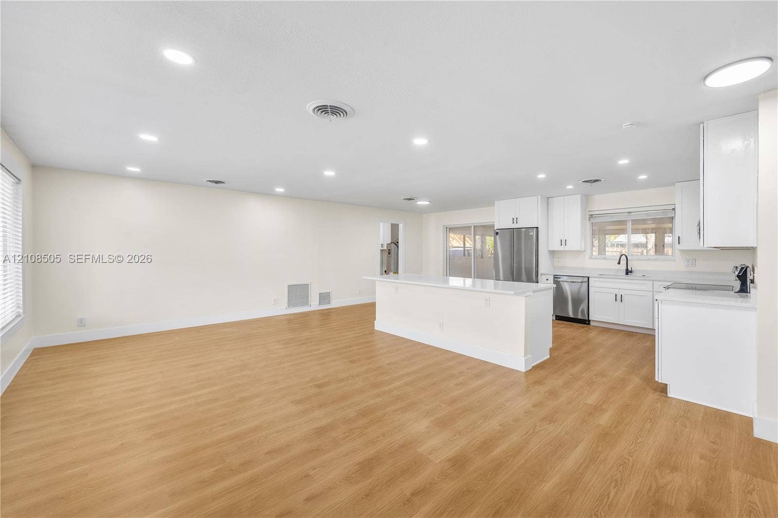 Open-concept interior featuring wood-finish flooring, recessed lighting, and a kitchen equipped with white cabinetry, quartz countertops, and a stainless steel refrigerator