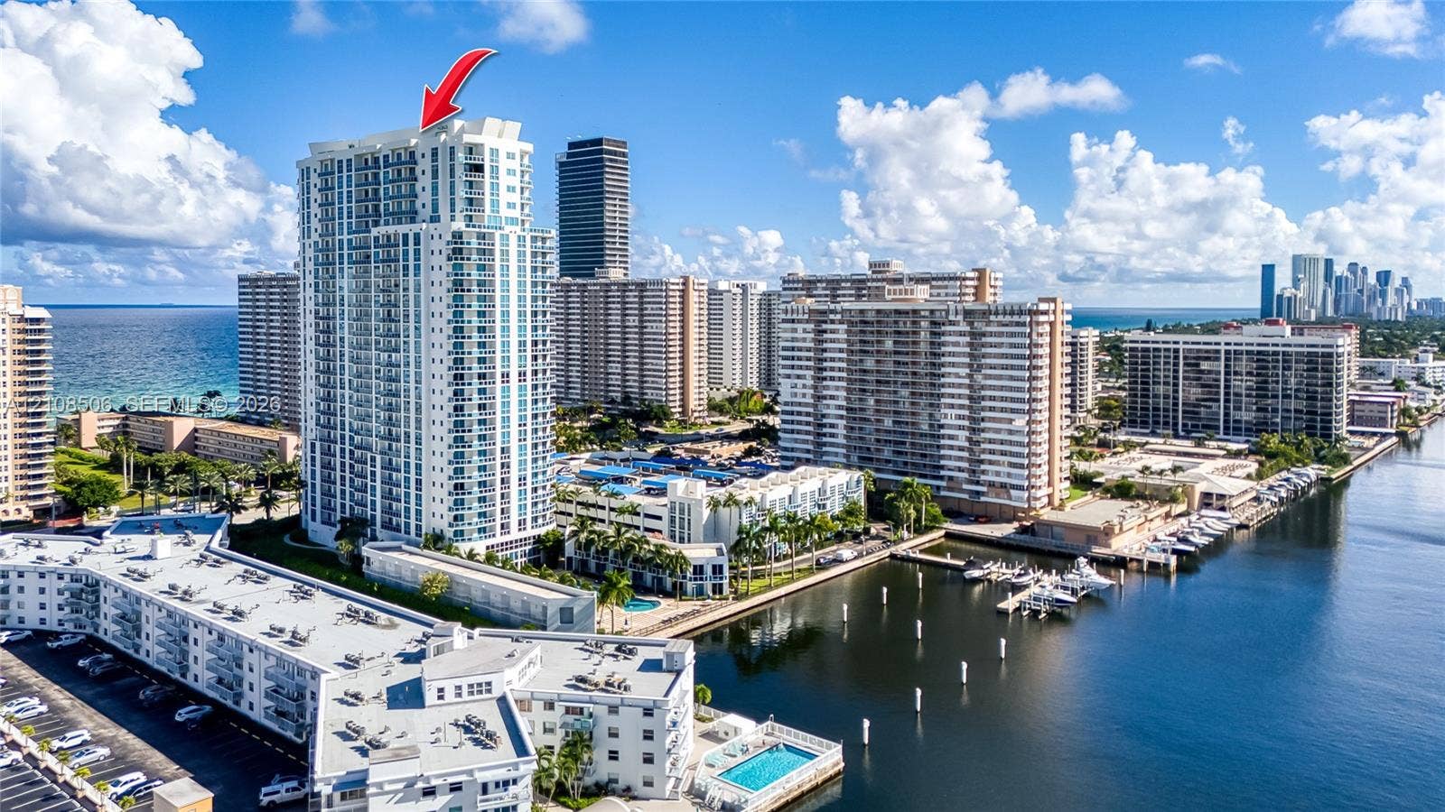 High-rise residential tower featuring multiple private balconies, floor-to-ceiling glass paneling, and an expansive concrete structure situated along the waterfront