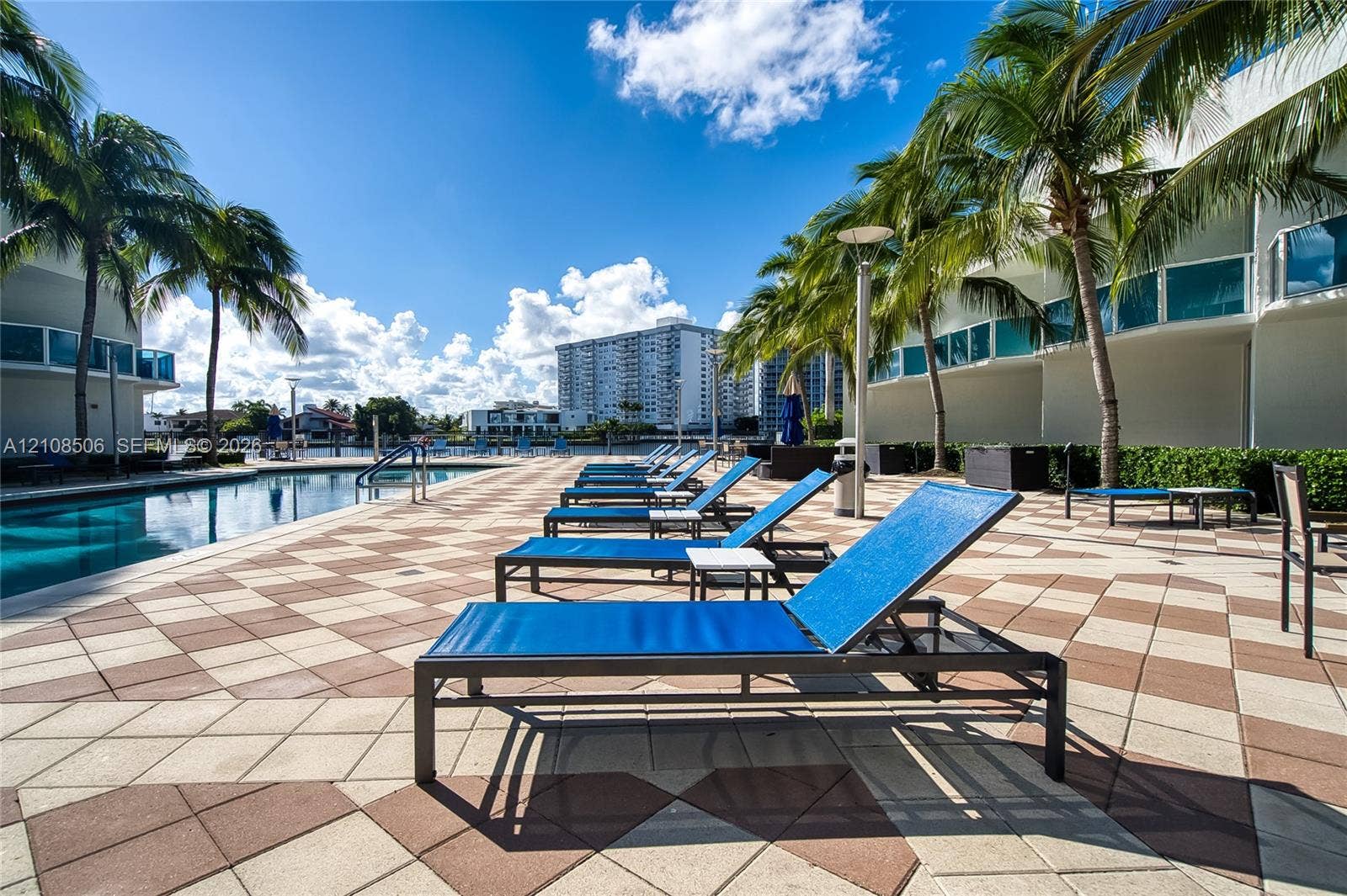 Swimming pool with geometric paver decking, surrounding palm trees, and waterfront bulkhead