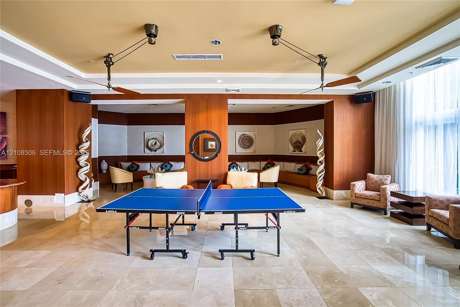 Open-concept common space featuring polished stone flooring, custom wood-panel wall treatments, integrated tiered ceiling lighting, and dual industrial-style ceiling fans