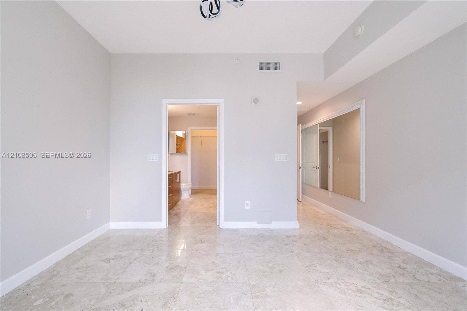 Interior room featuring neutral-toned stone-finish flooring, a large wall-mounted mirror, and a geometric flush-mount light fixture