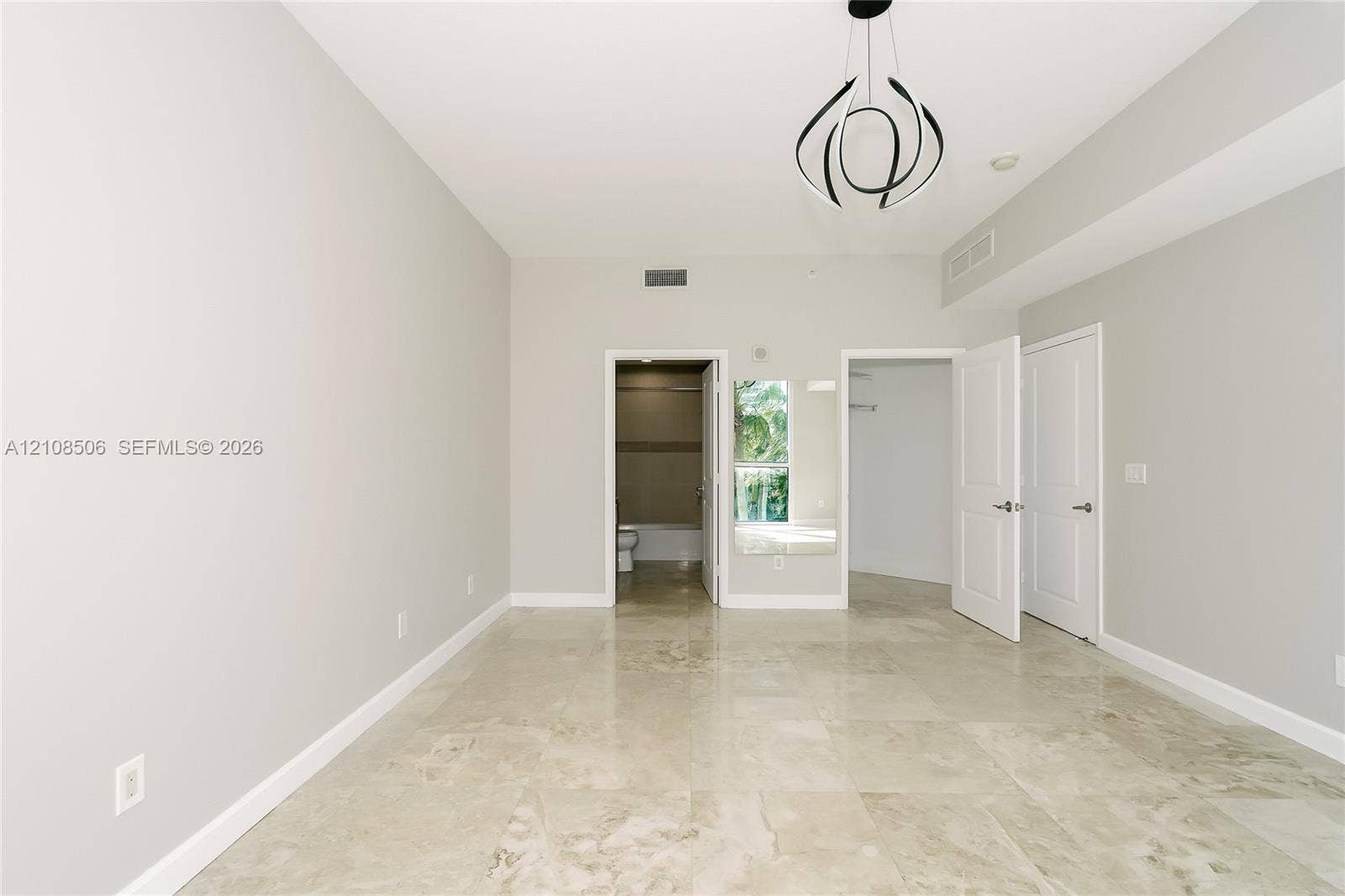 Neutral-toned room featuring large-format tile flooring, modern sculptural pendant lighting, and multiple interior door entries with panel detailing