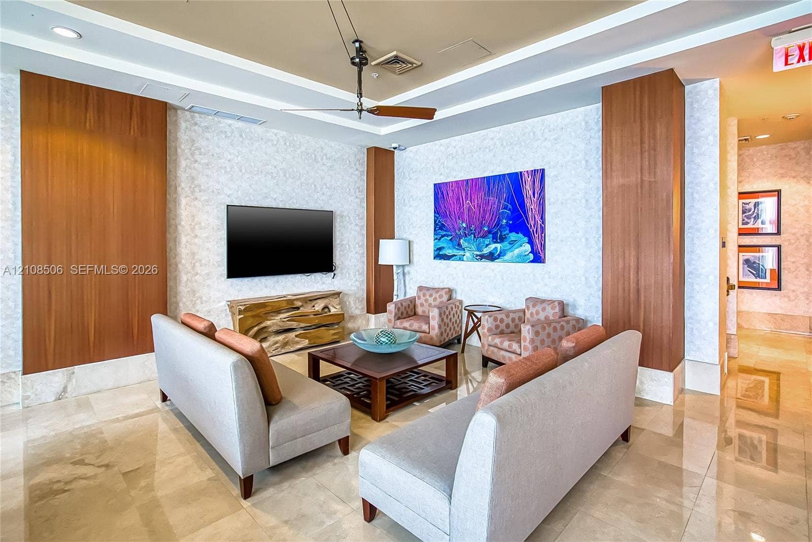 Polished stone flooring, custom wood-paneled wall accents, recessed lighting with tiered tray ceiling, and a modern industrial-style ceiling fan