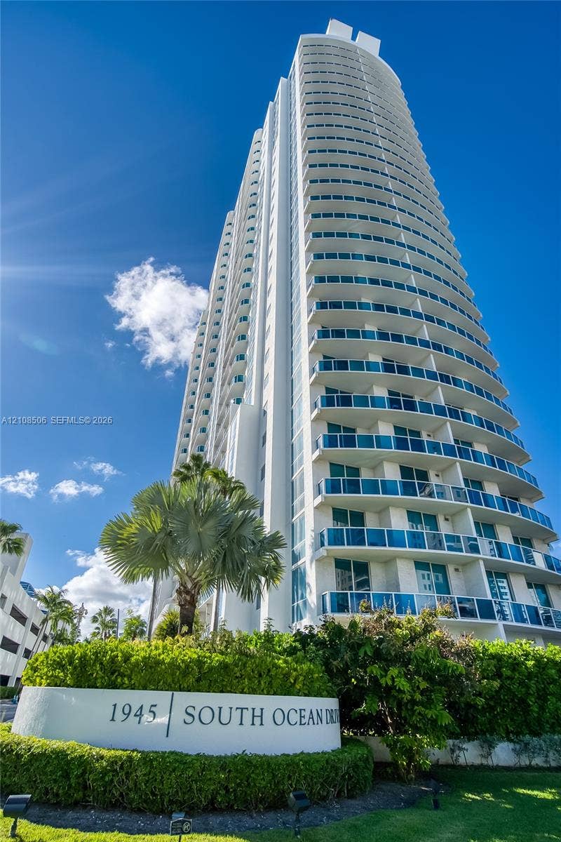 High-rise tower featuring tiered glass balconies, smooth white facade, and landscaped grounds with mature palm trees