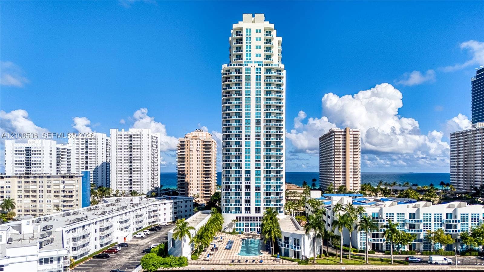 High-rise residential tower featuring tiered glass balconies, an expansive ground-level swimming pool, and stone-paved pool deck