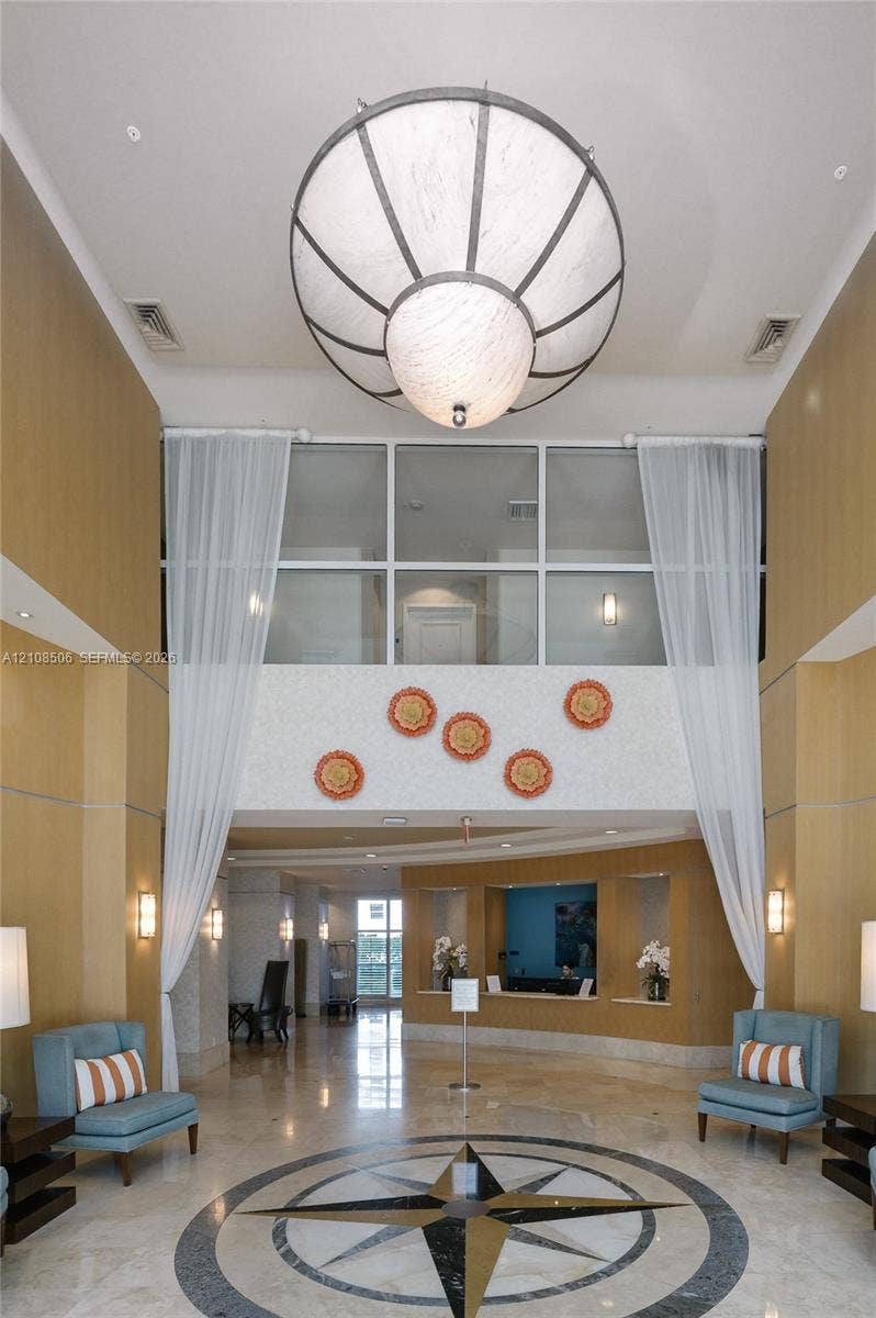Grand entrance lobby featuring double-height ceilings, a large spherical pendant light, stone flooring with an inlaid compass rose medallion, wood-paneled walls, and a built-in reception desk
