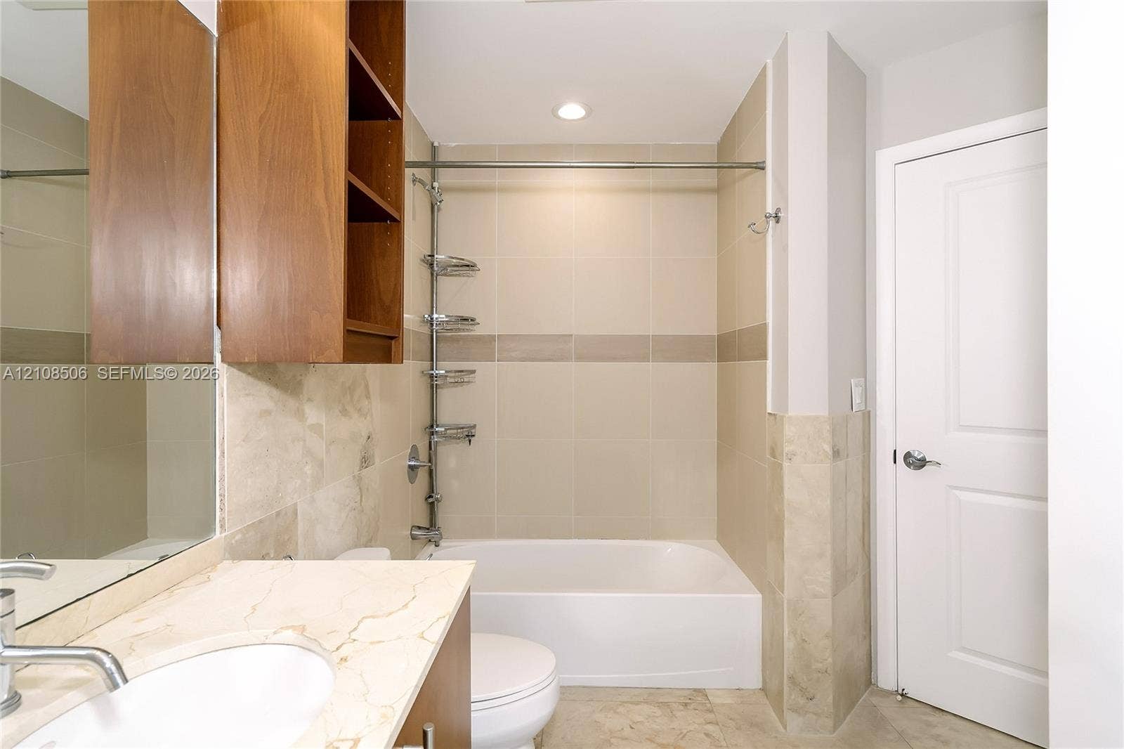 Bathroom featuring wood-finish cabinetry, stone-surface vanity countertop with an integrated basin, floor-to-ceiling tile surround, and built-in shelving