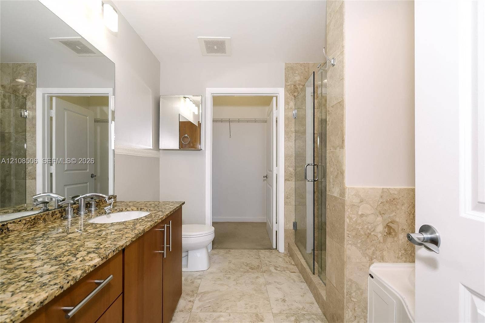 Bathroom featuring a vanity with stone-finish countertop, undermount sink, shower with glass enclosure and stone-finish tile surround, and tile flooring