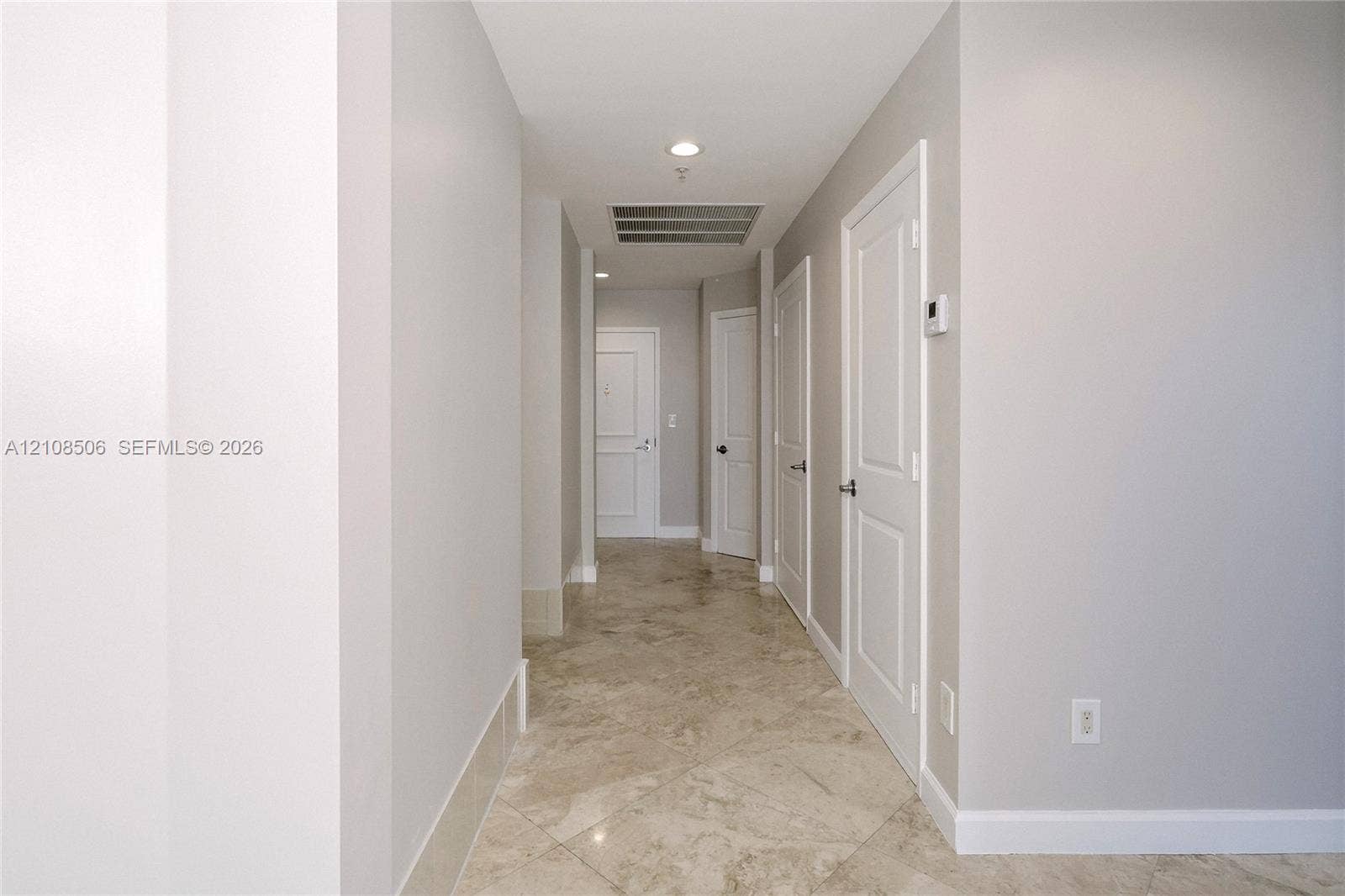Hallway featuring diagonal-set stone-finish flooring, recessed lighting, and multiple interior paneled doors with metal hardware
